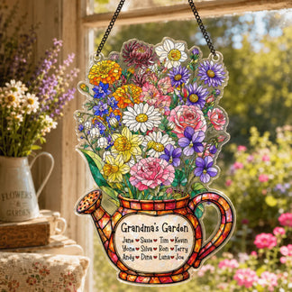 A vibrant, flower-filled watering can decoration, featuring a 'Grandma's Garden' label, hangs in a sunny window with a metal pitcher of flowers nearby.