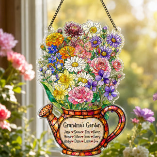 A clear acrylic watering can decoration, filled with a vibrant bouquet of various flowers, hanging by chains in a sunny window. The base reads "Grandma's Garden" with names.