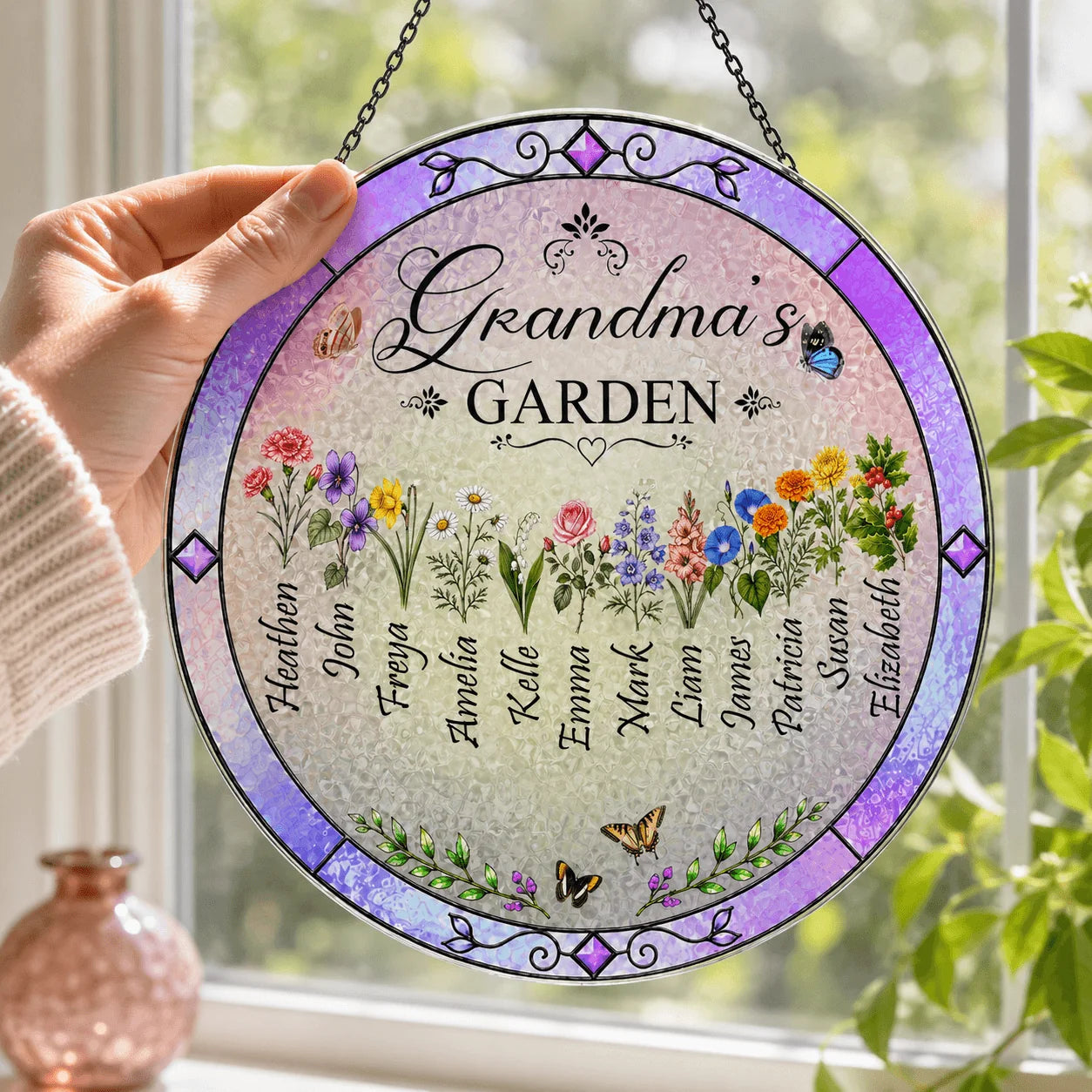 Decorative round sign with floral designs and names, held in front of a window with plants.