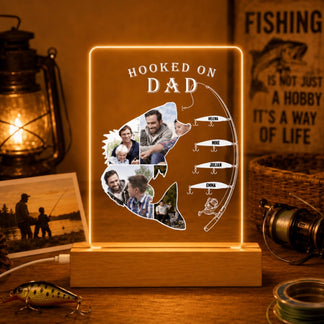Personalized light-up sign shaped like a fish with family photos and 'Hooked on Dad' text, surrounded by fishing-themed decor.