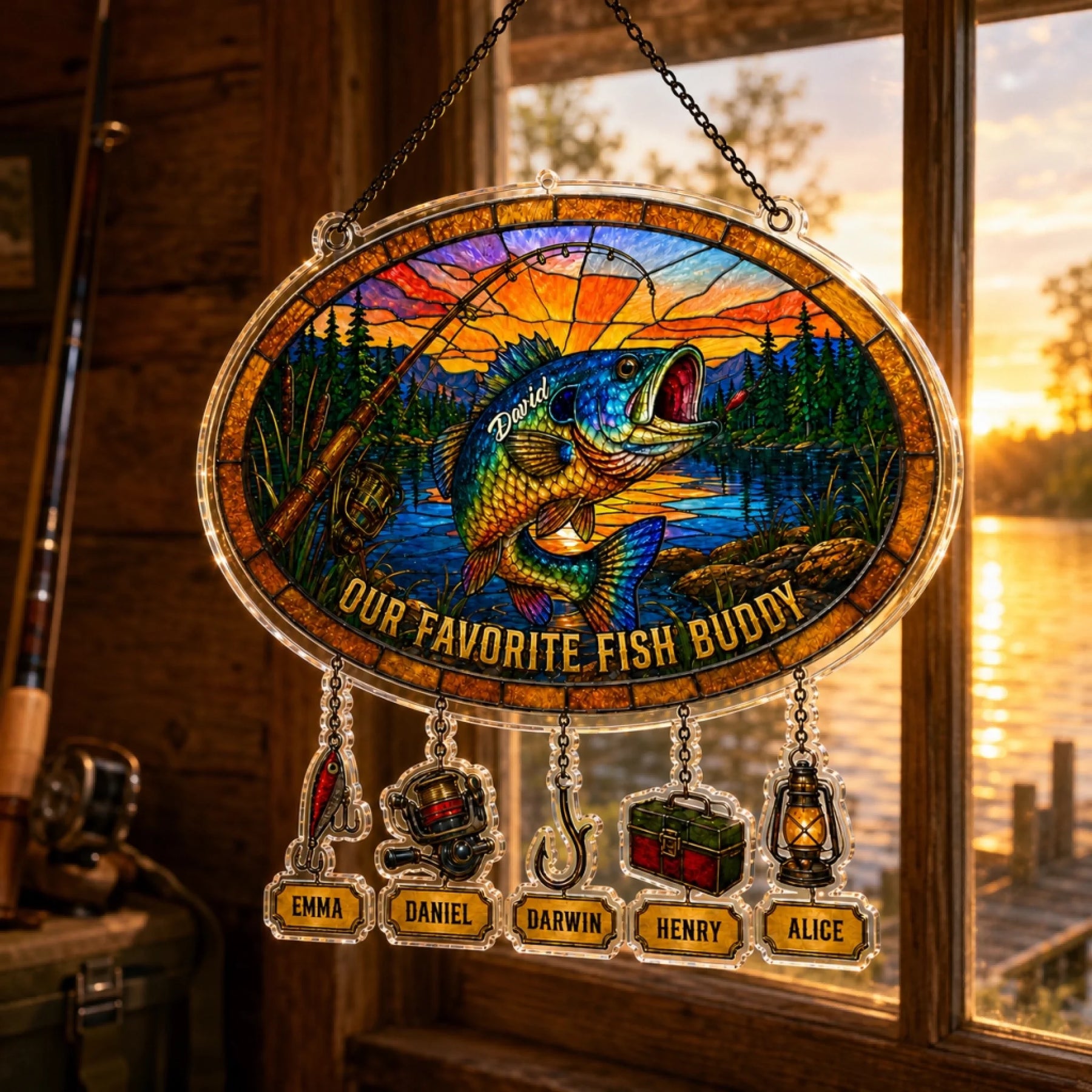 Stained glass panel with fish design and names, hanging by a window with a sunset view.