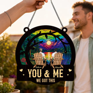Decorative sign with two people in chairs, rainbow design, and text 'You & Me We Got This' held by a person outdoors.