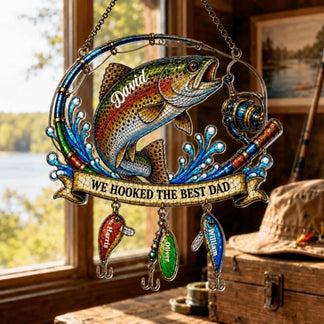 Decorative fishing-themed ornament with a rainbow trout and 'We Hooked the Best Dad' text, placed indoors near a window.