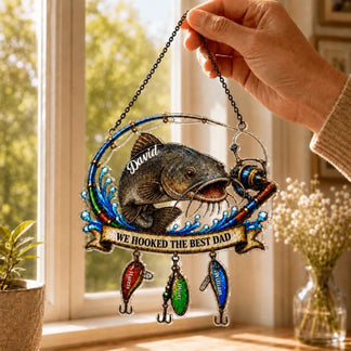 Decorative fishing ornament with engraved text held by a hand in a home setting.