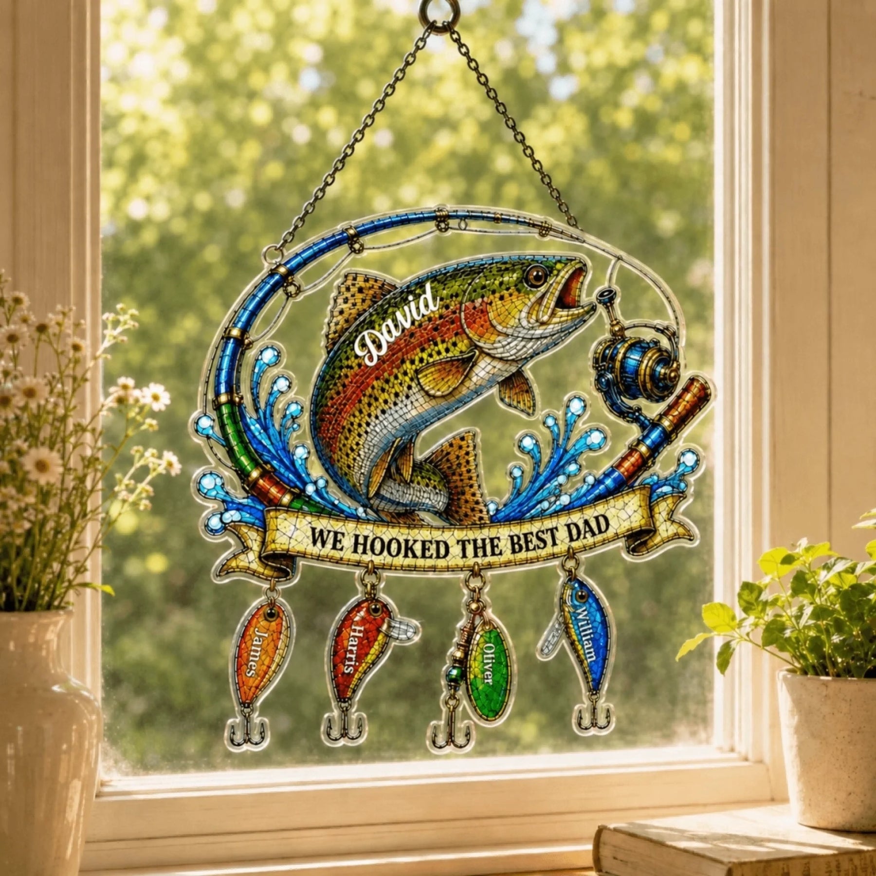 Decorative stained glass panel with a fish and text 'We hooked the best dad' hanging by a window.