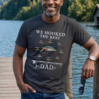 Man wearing a t-shirt with 'We Hooked the Best Dad' design by a lake.
