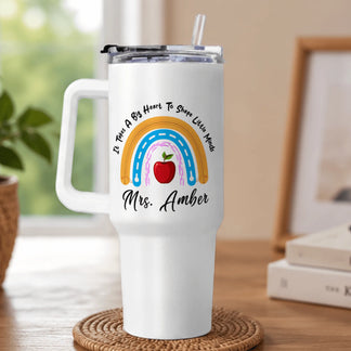 White tumbler with rainbow, apple, and text design on a wooden surface.
