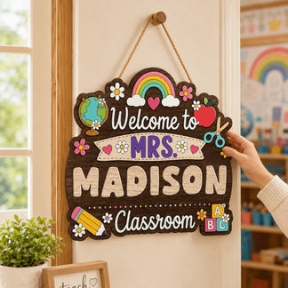 Decorative classroom sign with 'Welcome to Mrs. Madison Classroom' text, colorful graphics, and a hand holding it.