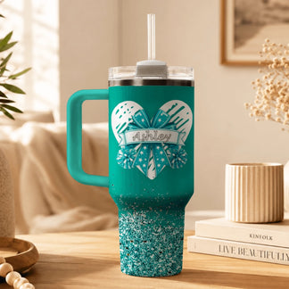 A personalized teal tumbler for cheerleaders decorated with a heart bow design and the name Ashley printed in black.