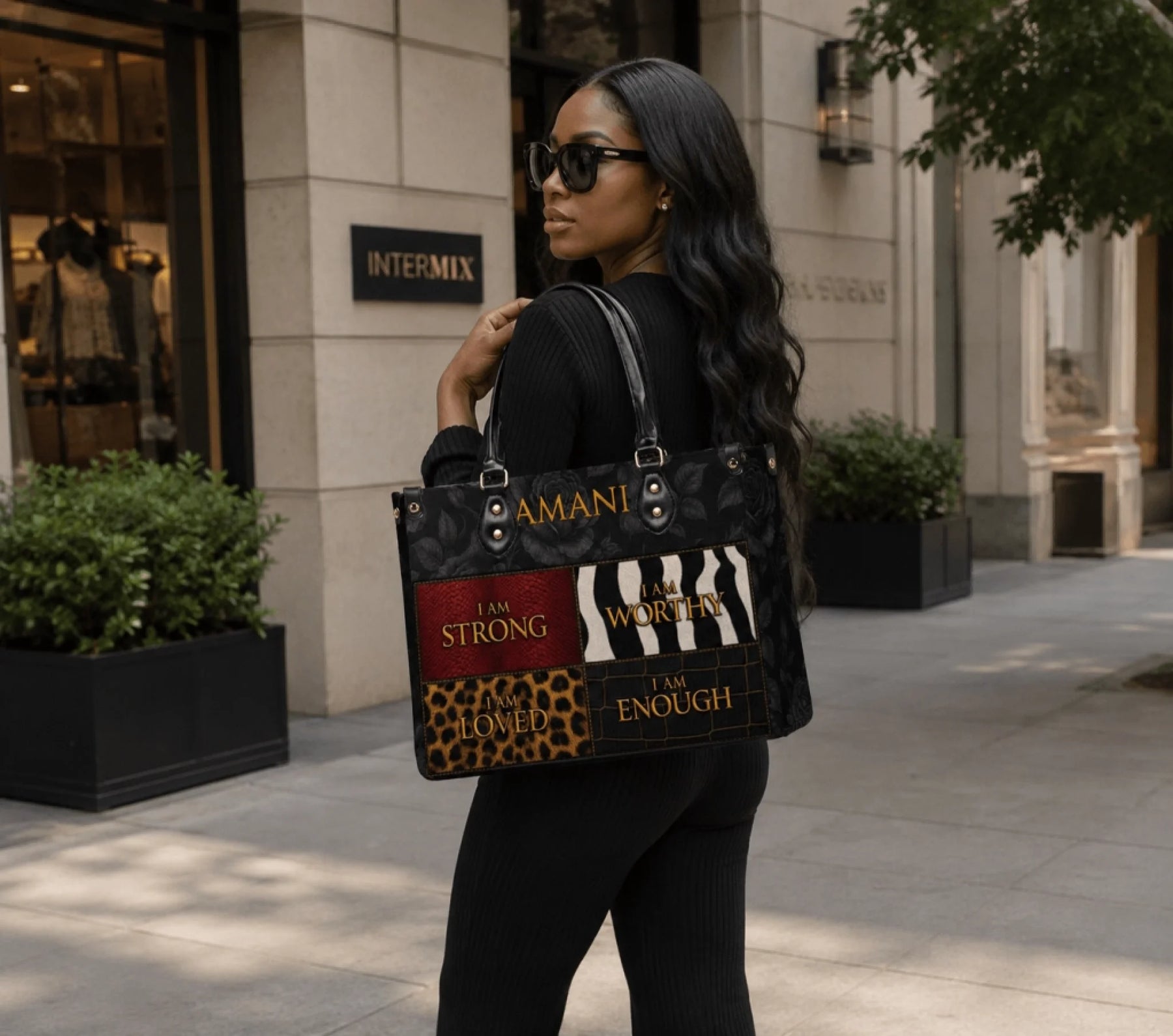 A stylish black PU leather tote bag featuring the name Amani and daily affirmation prints, held by a woman on a street.