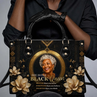 Close up of a personalized black queen tote bag with gold floral art and empowering quotes held by a woman wearing black gloves.