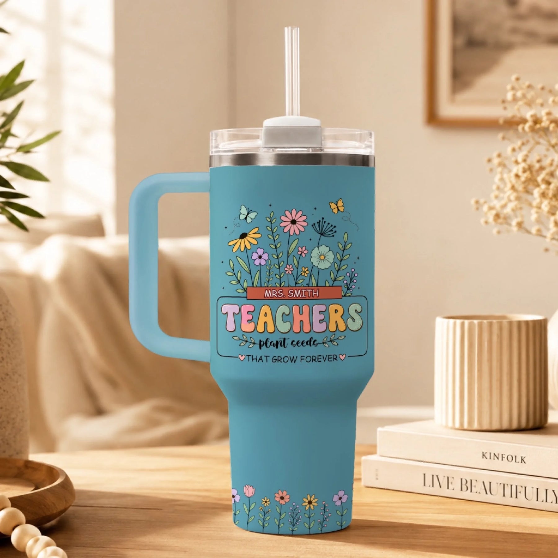 Single light blue insulated teacher tumbler with straw, floral garden art and custom name plate on table.