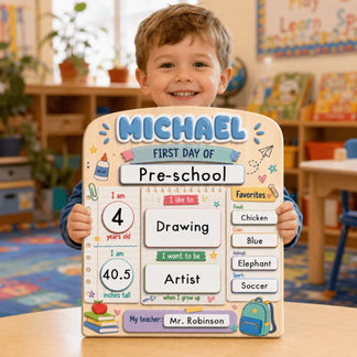 Happy preschool boy holding a custom wooden back to school board with his name, age, interests, and teacher details.