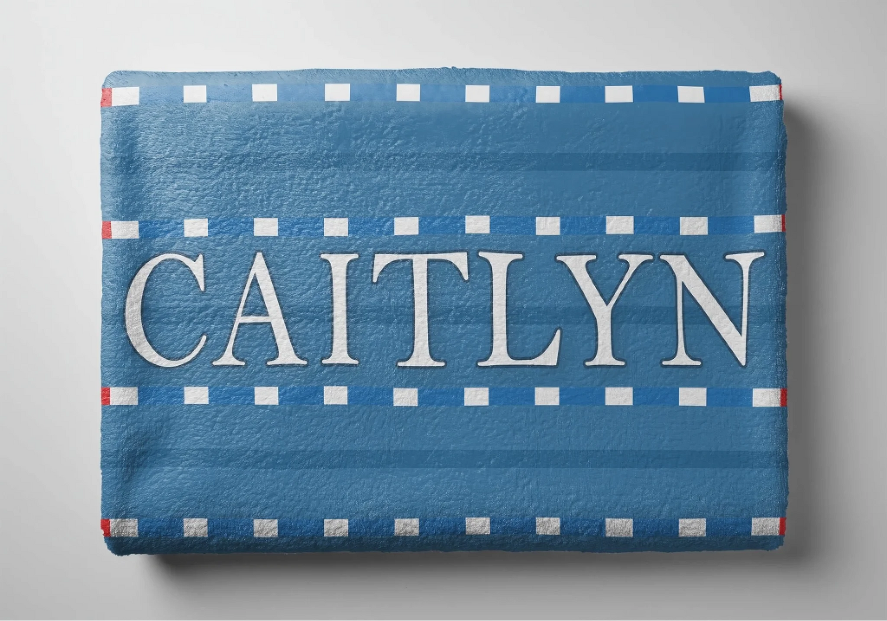 Folded personalized beach towel with a blue swim lane and white line pattern featuring the custom name Caitlyn.