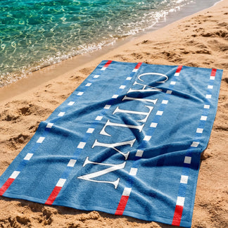 Personalized blue swimming pool lane beach towel with the name Caitlyn, displayed on a sandy beach by the water.