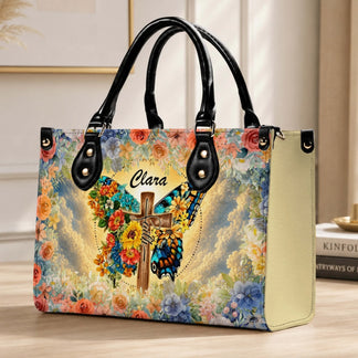 Elegant handbag personalized with the name Clara, featuring a serene butterfly and cross art piece surrounded by a lush floral pattern.