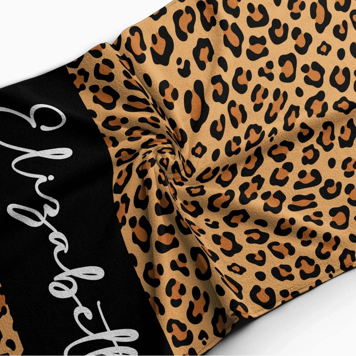 A close up view of a personalized leopard print beach towel with the name Elizabeth on a black central stripe