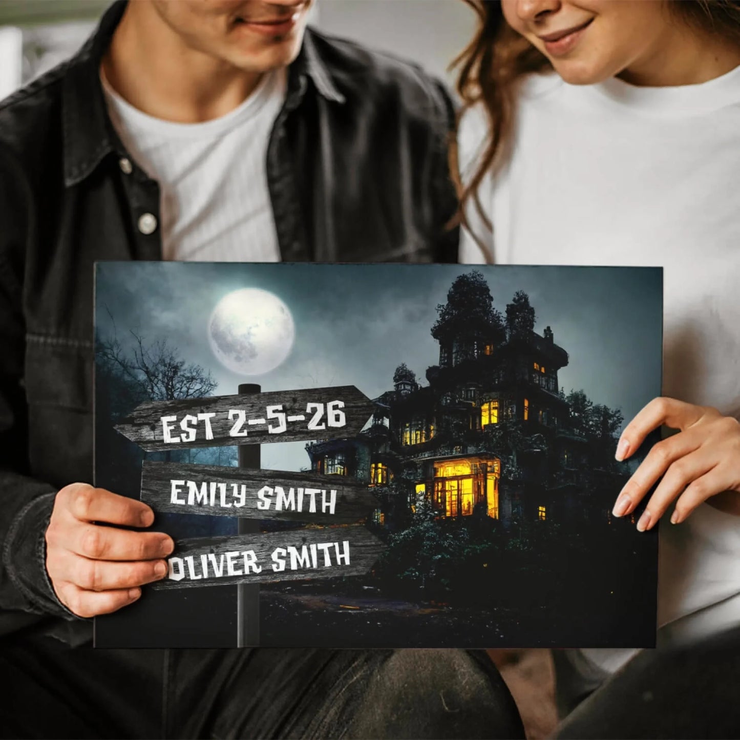 A couple holding a custom spooky haunted house canvas sign featuring personalized names for a romantic gift.