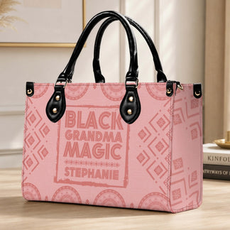 A custom Black Grandma Magic handbag with pink patterned fabric and black leather accents displayed on a wooden desk surface.