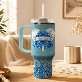 A light blue insulated tumbler featuring a cheering themed heart and bow illustration with the custom name Ashley.