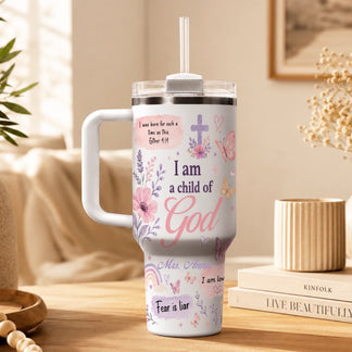 White personalized tumbler with 'I am a child of God' text, floral motifs, and a cross, set in a cozy home environment.
