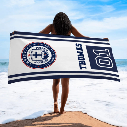 A personalized beach towel for Christian School Academy featuring a crest, the name Thomas, and the number 01 on white.