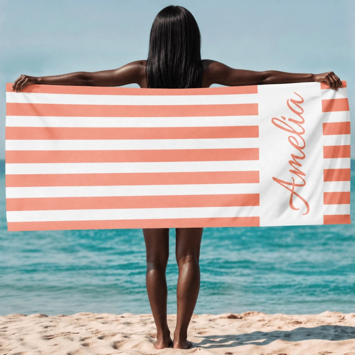 A personalized beach towel featuring coral and white horizontal stripes with the custom name Amelia in script.