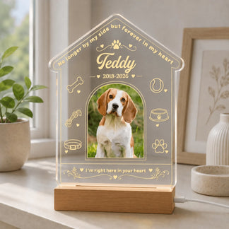 A lighted house-shaped acrylic keepsake with a photo, pet icons, and memorial text on a desk.