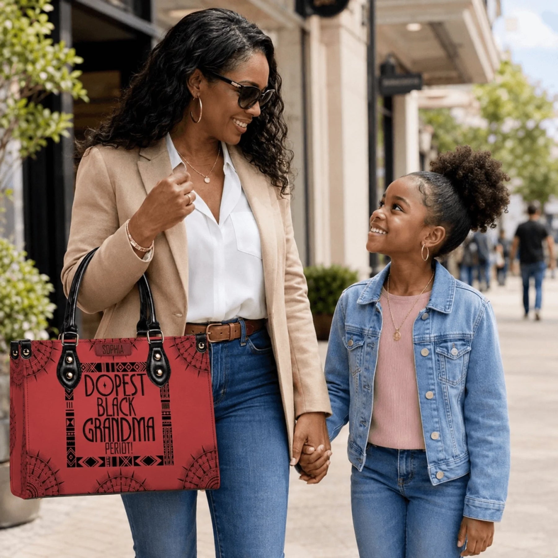 Woman holding a custom red handbag that says Dopest Black Grandma Period while standing next to a young girl.