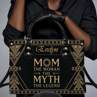 Close up of a personalized black and gold handbag with the text Mom The Woman The Myth The Legend held by a person.