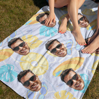 A personalized beach towel with a custom photo pattern being used on a grassy lawn with person legs visible.