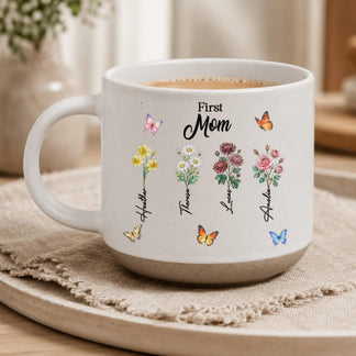 Close-up of a white custom mug featuring four flower stems, butterflies, and the text First Mom with floral names.