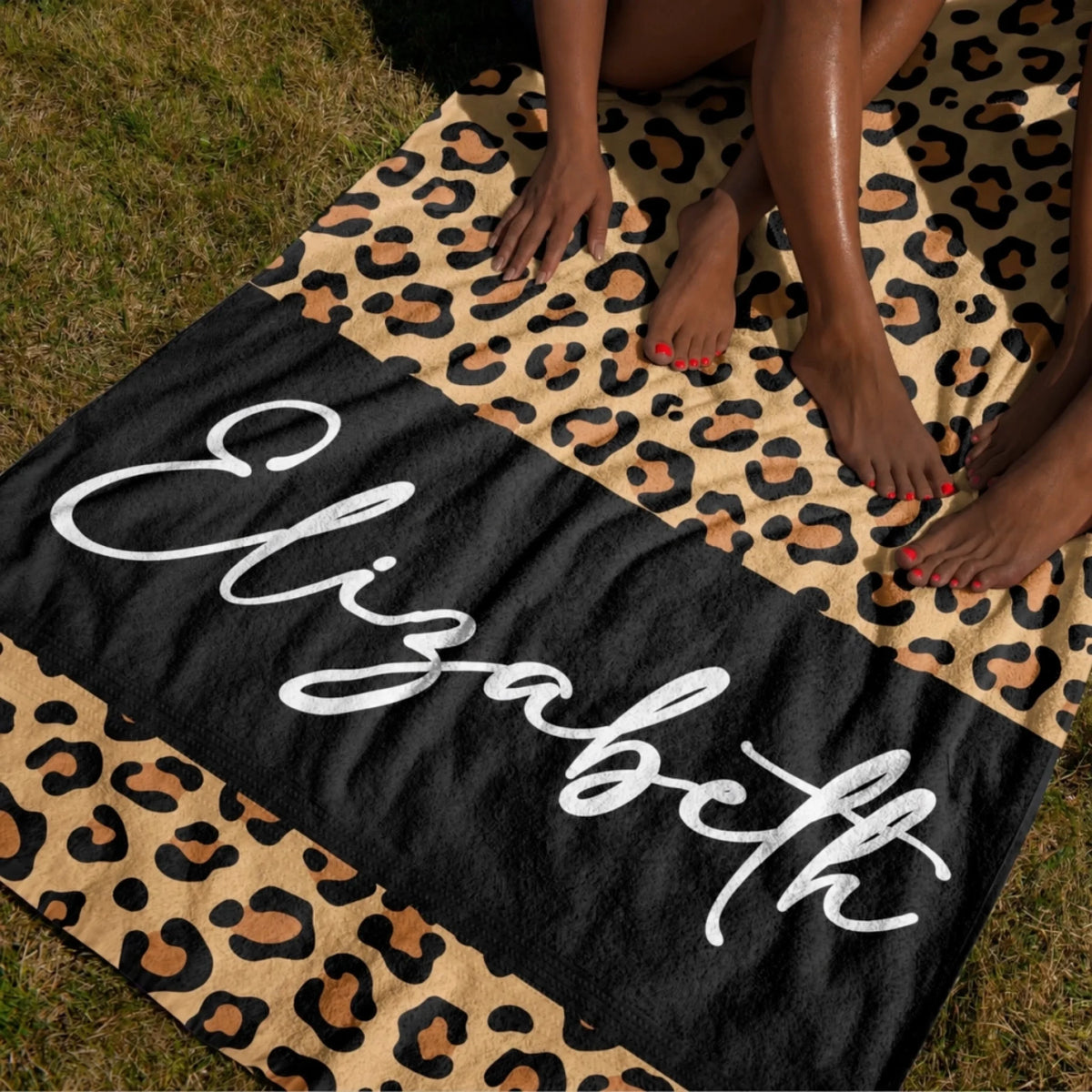 Personalized leopard print towel with the name Elizabeth displayed on a black background, laid out on outdoor grass.