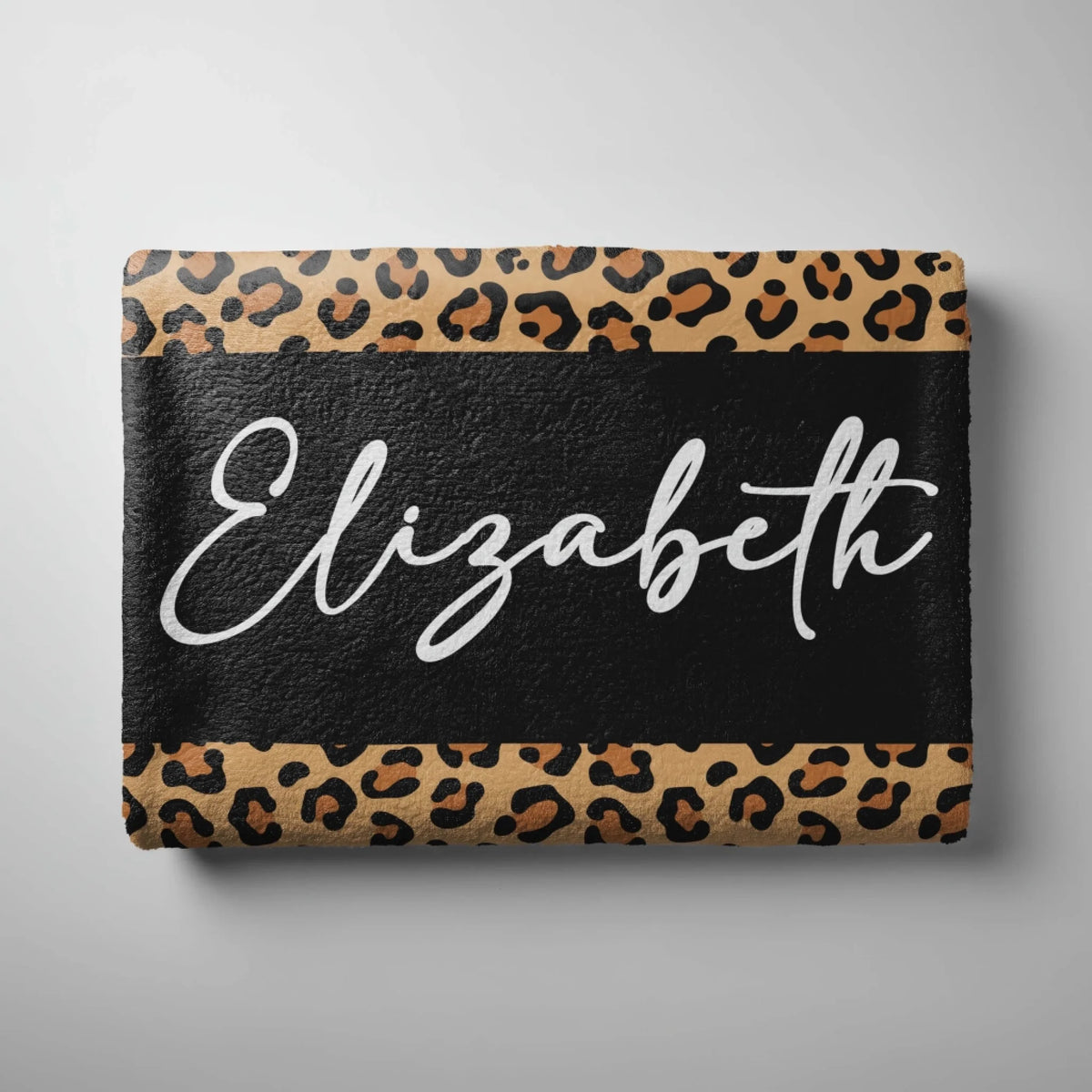 A folded personalized leopard print beach towel displaying the name Elizabeth printed in stylish white script font