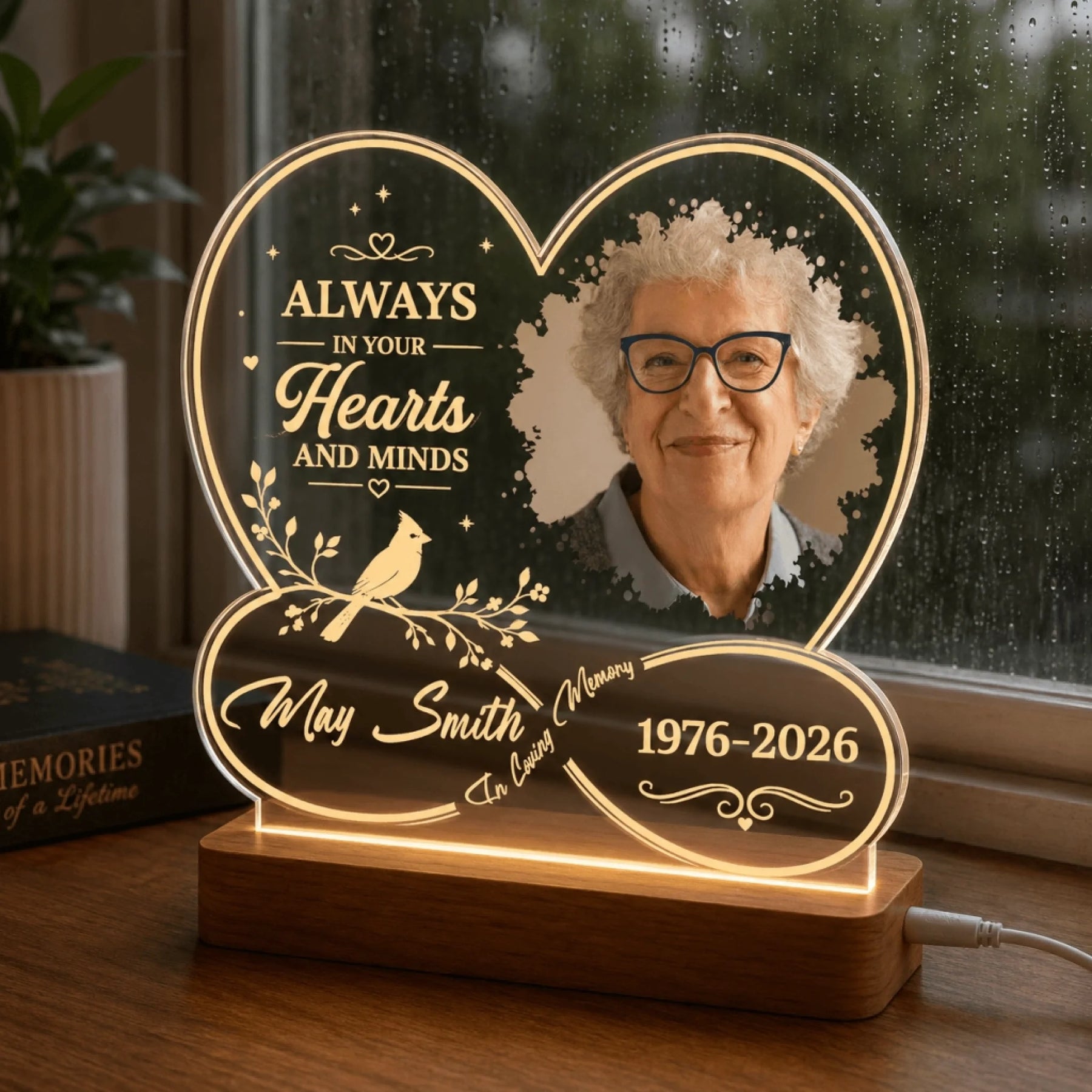 Decorative heart-shaped memorial LED light with custom photo and dates displayed on a desk by a window.