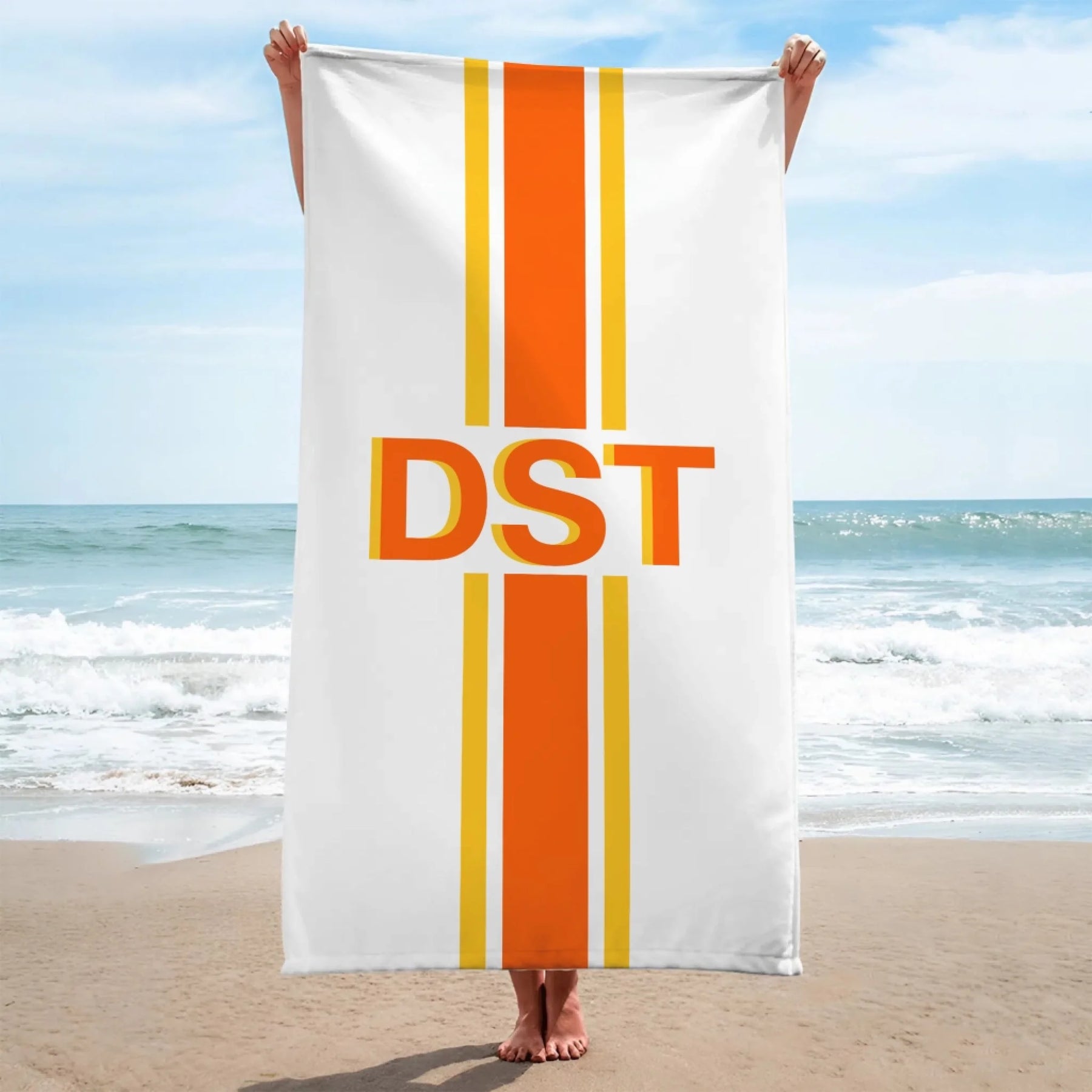 Woman holding a white and orange personalized beach towel with a DST monogram print standing on a sunny sandy beach