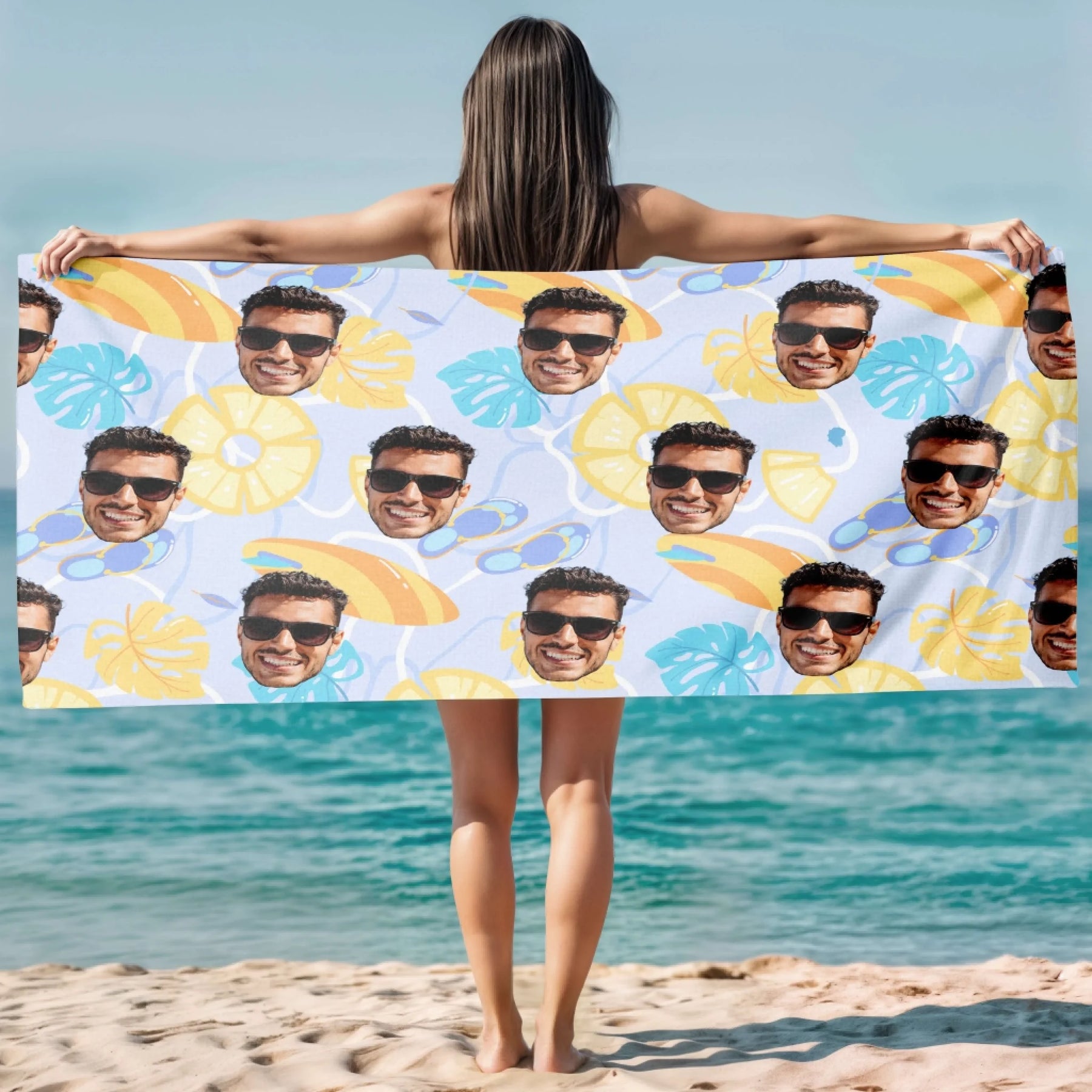 A woman holds up a personalized beach towel featuring a repeating photo pattern of a man wearing sunglasses for summer.