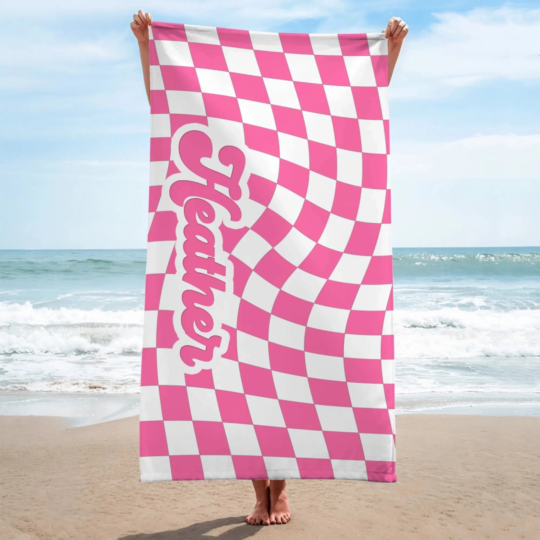 A vertical beach towel displaying a pink and white wavy checkered design and the name Heather in a custom script font.