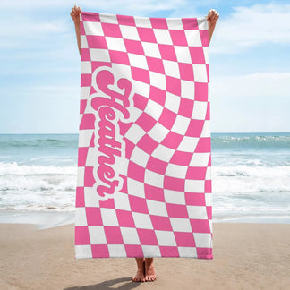 A vertical beach towel displaying a pink and white wavy checkered design and the name Heather in a custom script font.