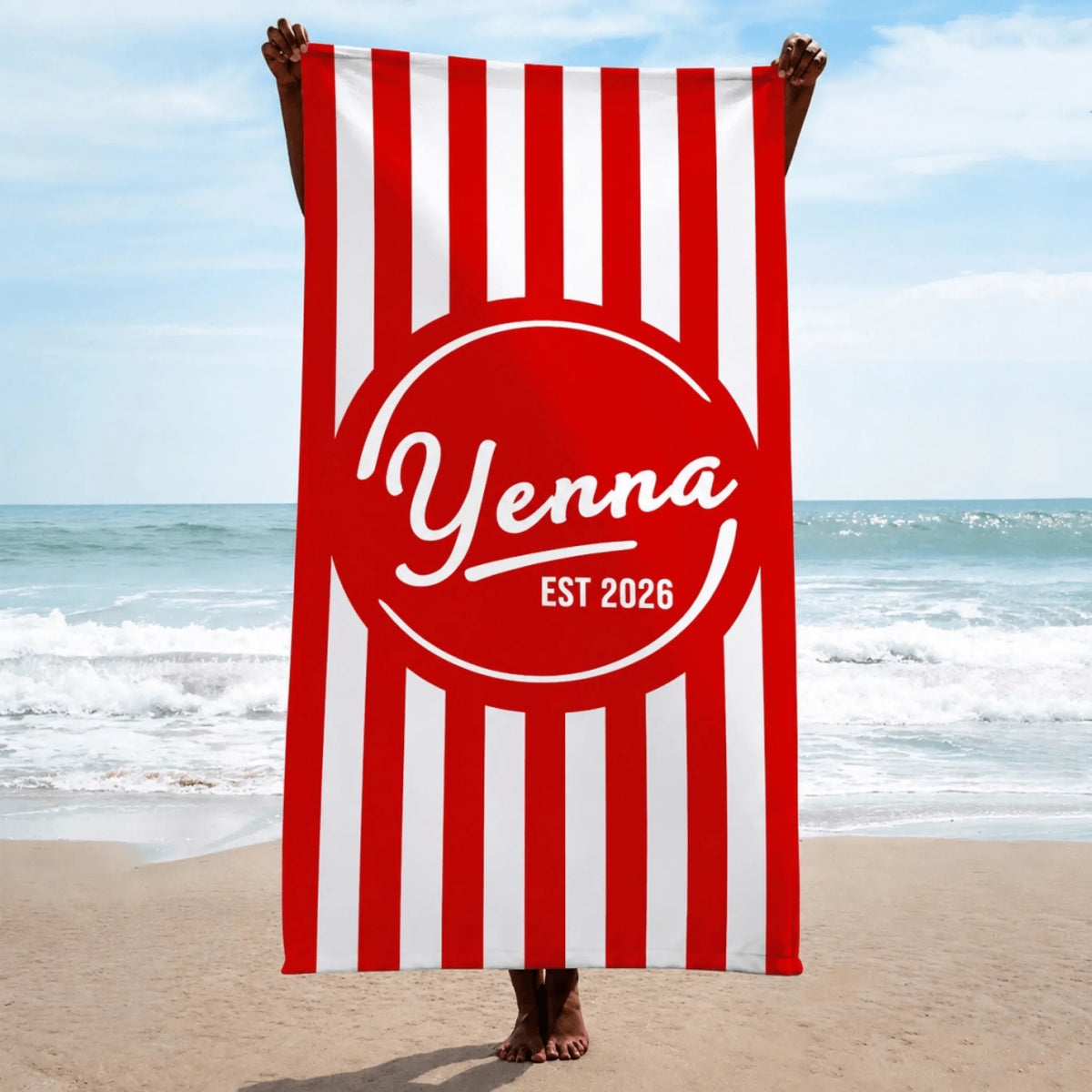 A person holding up a custom red and white striped beach towel that displays the name Yenna and the year 2026.