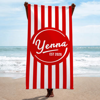 A person holding up a custom red and white striped beach towel that displays the name Yenna and the year 2026.