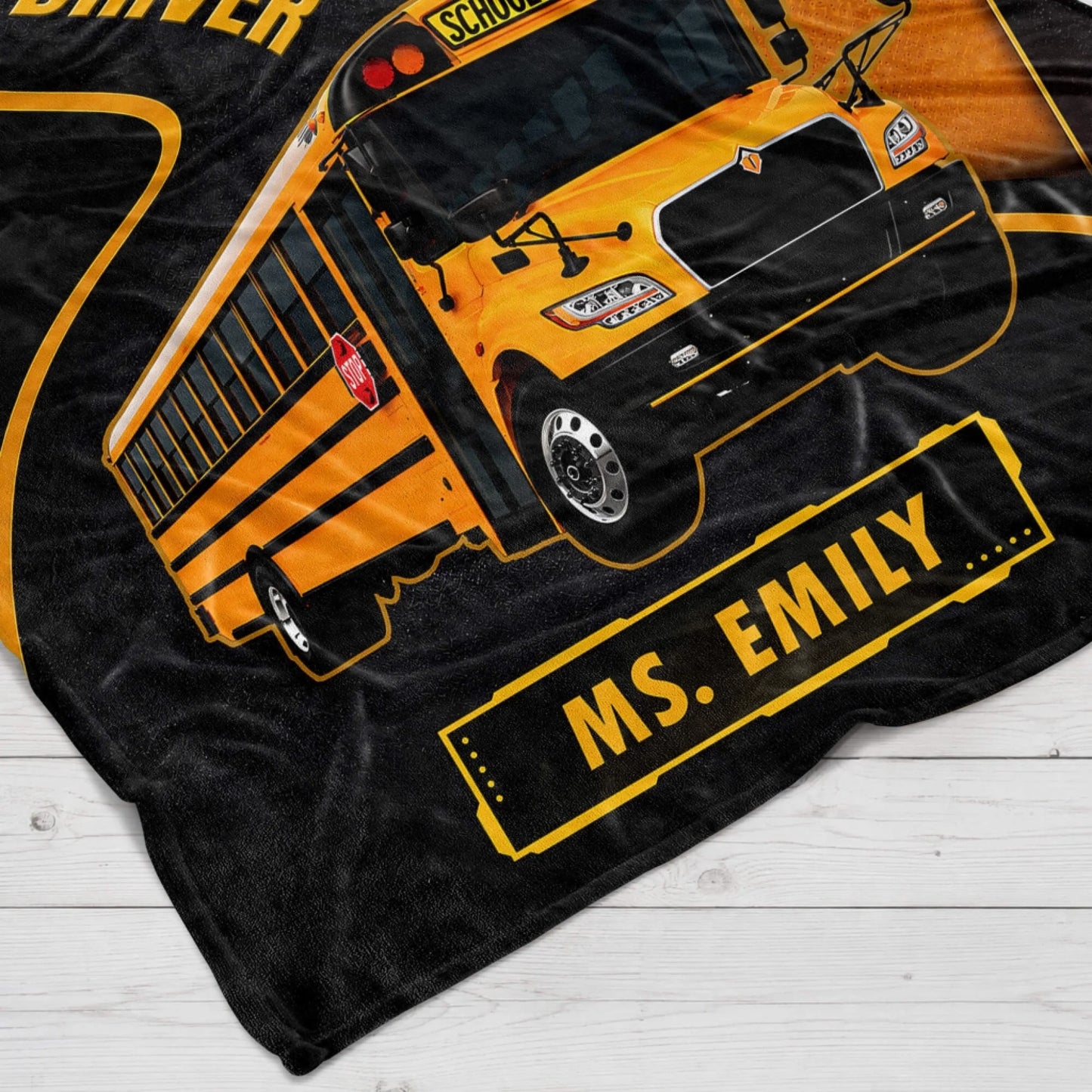 Close up of a personalized school bus blanket with the name Ms. Emily printed on a yellow bus driver themed design.