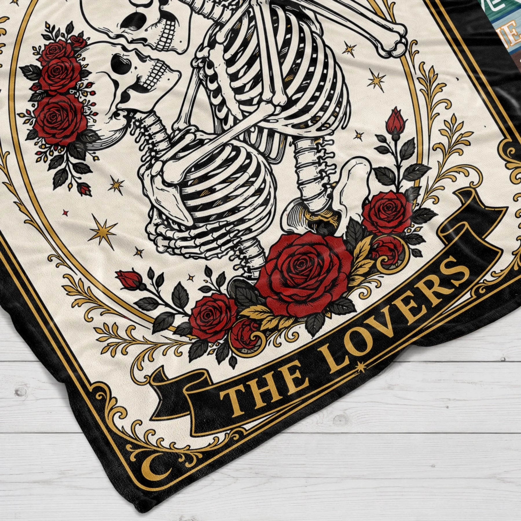 Close up of a romantic tarot card themed blanket featuring skeletons dancing surrounded by red roses and gold trim.