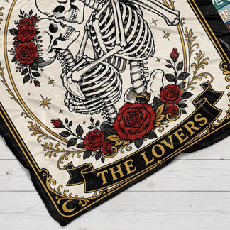 Close up of a romantic tarot card themed blanket featuring skeletons dancing surrounded by red roses and gold trim.