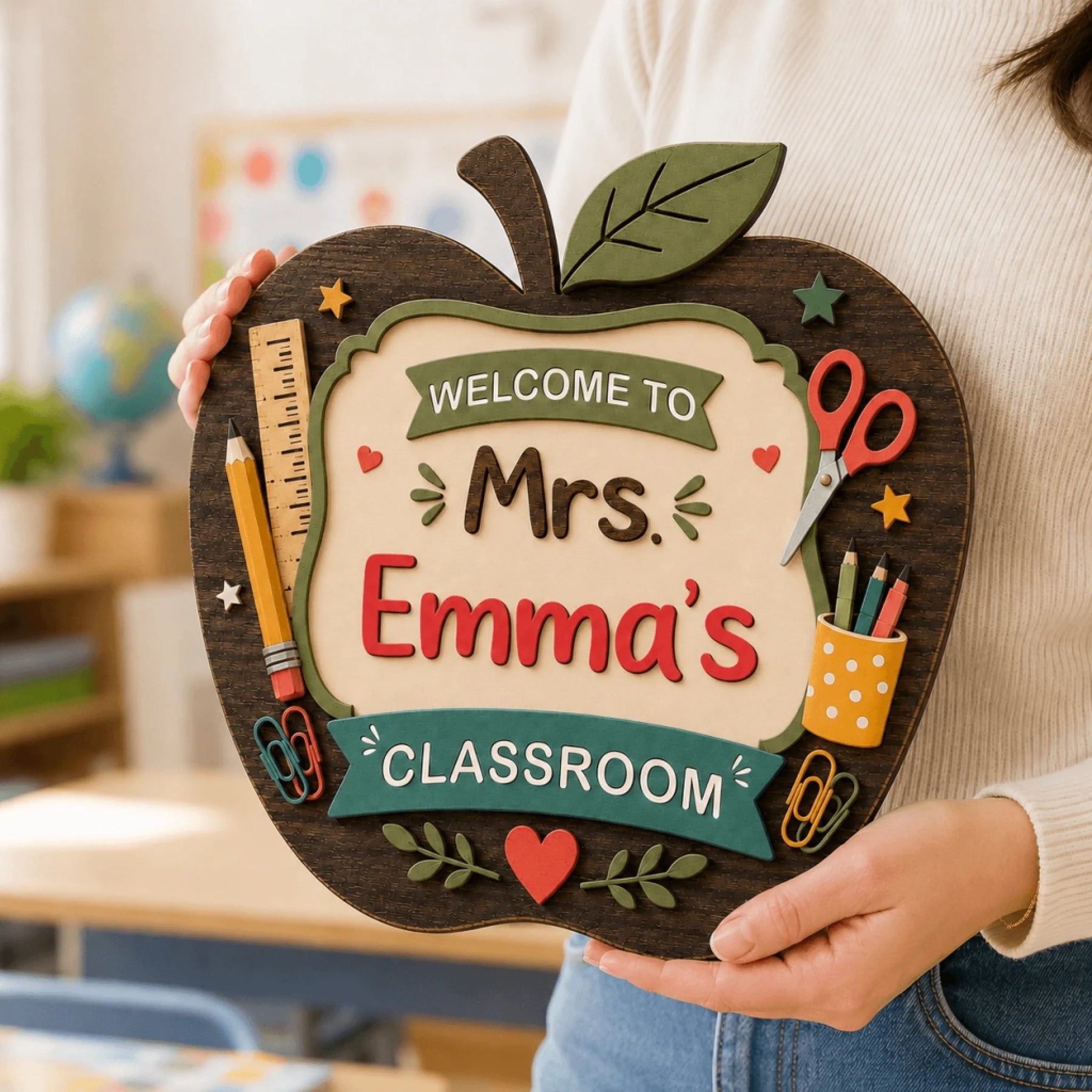 Person holding a personalized wooden apple sign that reads Mrs. Emma's Classroom in a classroom setting.