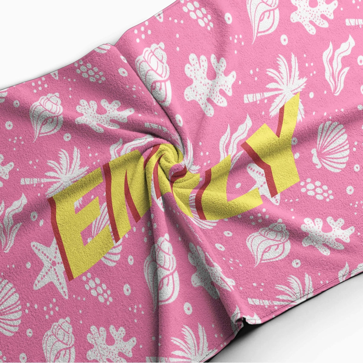 Close up of a personalized pink beach towel showing the name Emily over a fun tropical beach seashell pattern.