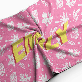 Close up of a personalized pink beach towel showing the name Emily over a fun tropical beach seashell pattern.