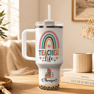 Personalized teacher life tumbler on a table featuring a leopard print rainbow design books and custom name.