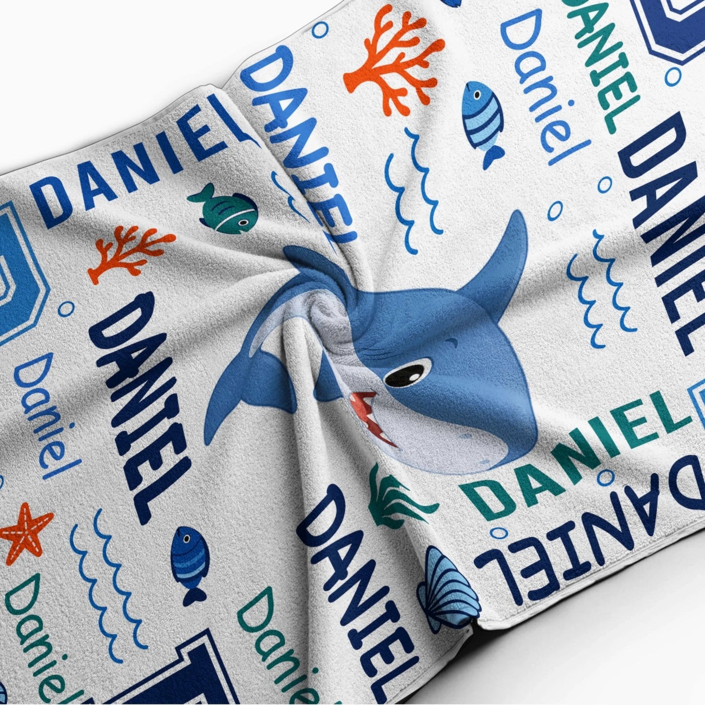 Close up of a personalized shark beach towel for boys with custom name text and fun blue ocean water illustrations.