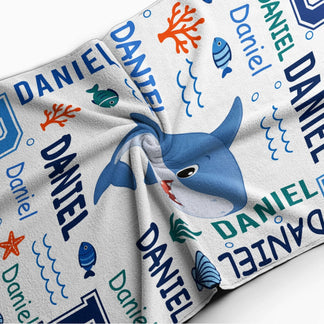 Close up of a personalized shark beach towel for boys with custom name text and fun blue ocean water illustrations.